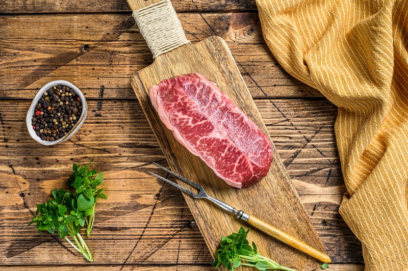 marbled beef on cutting board with herbs nearby