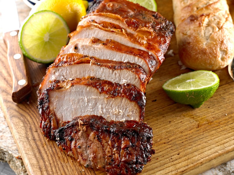 roasted pork tenderloin sliced on cutting board with bread and citrus garnish