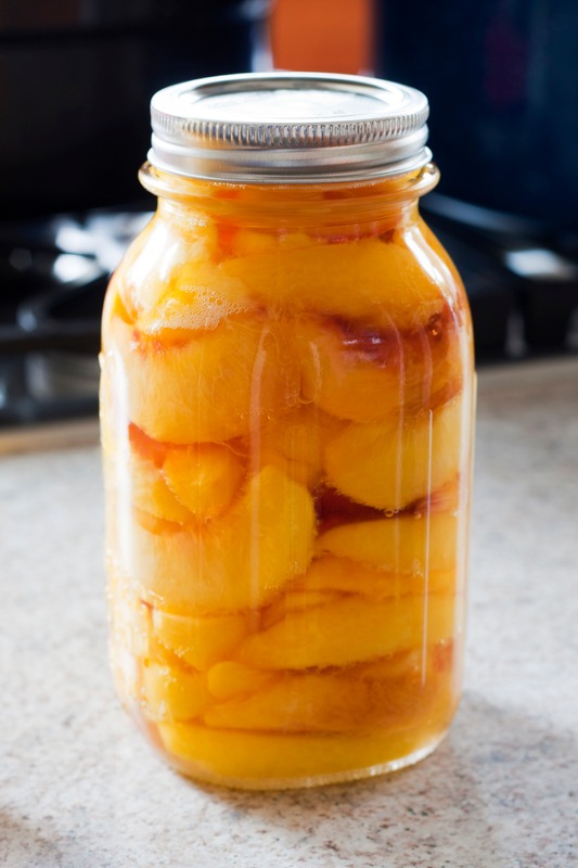 A canning jar full of peaches with canning pots in the background