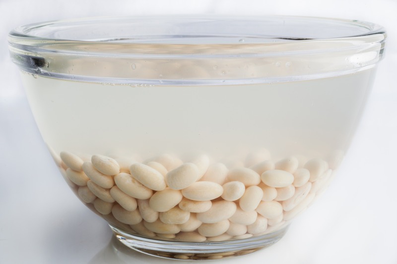 White beans soaked in water in glass bowl on white background