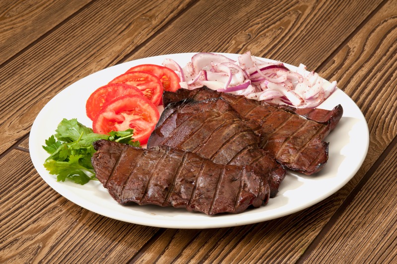 cooked beef liver with raw onions, tomatoes, and parsley on the side