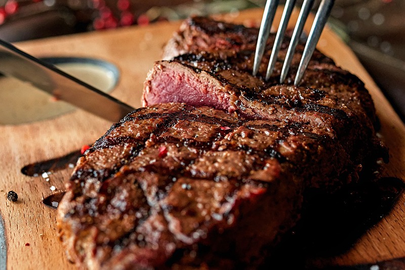 close up of fork and knife slicing into rare steak