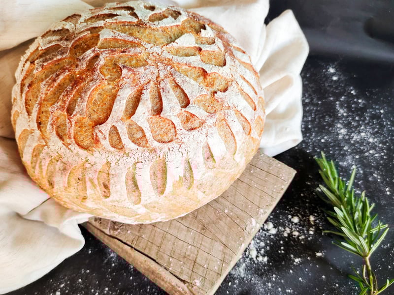 sourdough loaf on cutting board with fabric and rosemary garnish