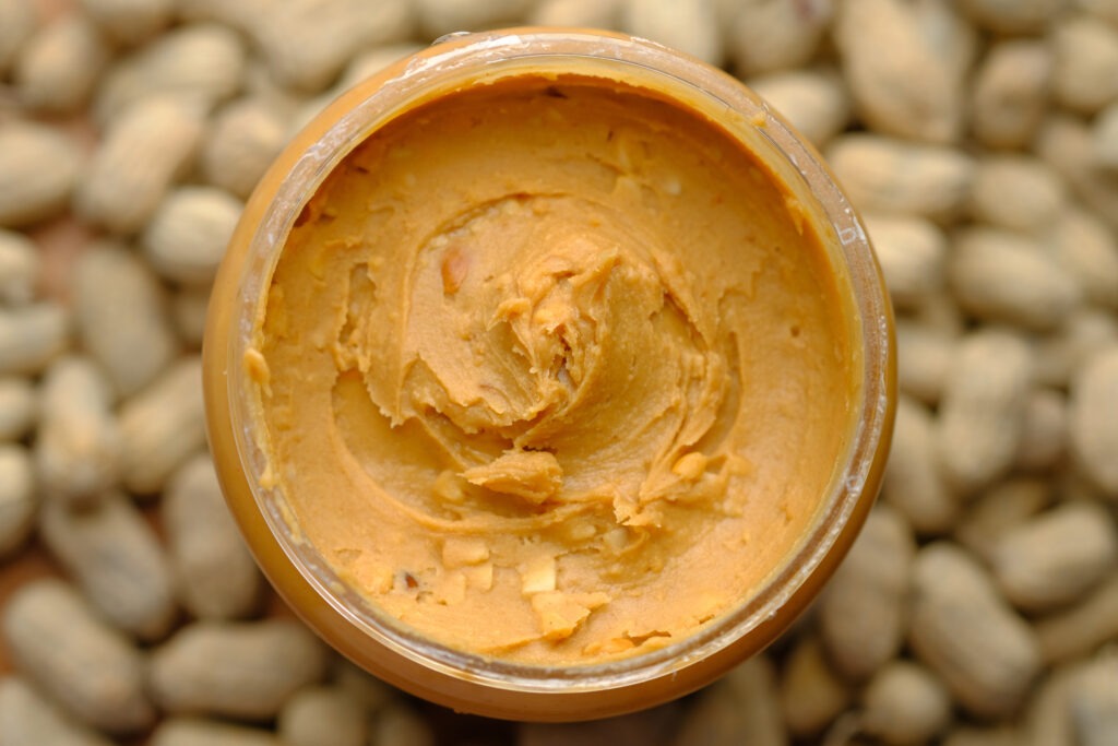 close up of homemade peanut butter in glass jar with peanuts in background