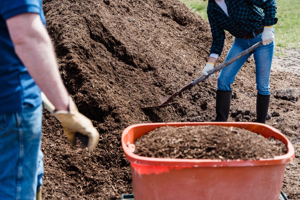a couple shoveling mulch into a wheel barrow